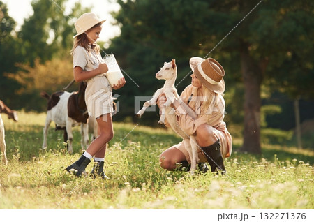 Glass with milk in hands. Mother and daughter are together on the farm with goats 132271376
