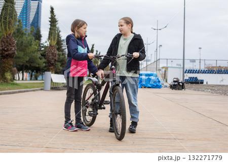 Full length portrait of young girls talking and walking together. Children with bikes outdoors 132271779