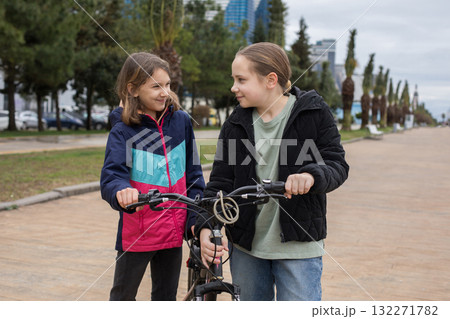 Cheerful children girls 10 and 12 years old with bicycle walking outdoors Cheerful children girls 10 and 12 years old with bicycle walking outdoors 132271782