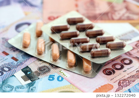 Thai baht currency money bills and medicine pills close up. The concept of medicine and pharmacy Thai baht currency money bills and medicine pills close up. The concept of medicine and pharmacy 132272040
