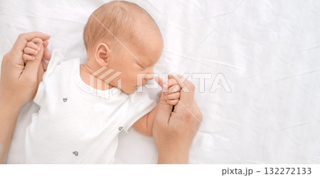 Newborn sweetly sleeping baby close-up on the bed. A mother holds her son by his delicate little hands 132272133