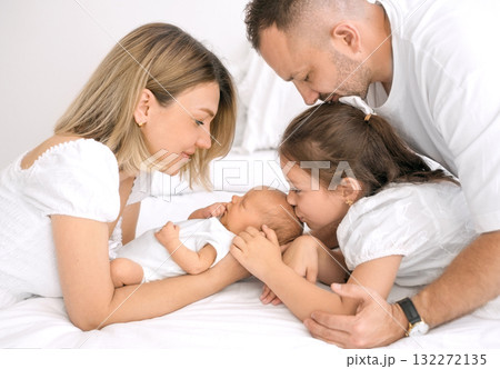 The older sister gently kisses her newborn brother. A baby surrounded by loving parents. The older sister gently kisses her newborn brother. A baby surrounded by loving parents. 132272135
