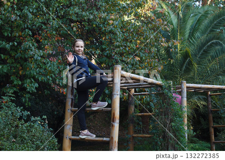 Young Girl Climbing on a Wooden Playground in Public Park, Enjoying Outdoor Activities and Nature Young Girl Climbing on a Wooden Playground in Public Park, Enjoying Outdoor Activities and Nature 132272385