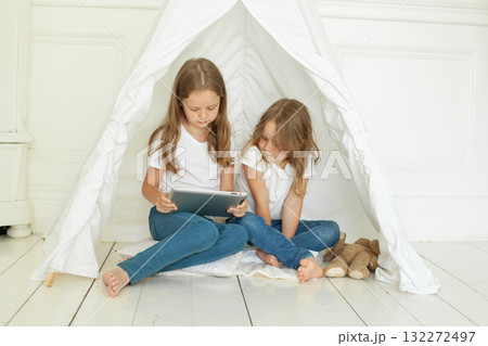 Cute little girl sisters with tablet pc computer in kids tent at home. Childhood, technology  132272497