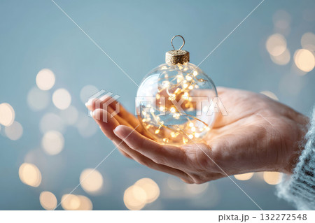 Hand holding glowing ornament glass ball fairy light festive holiday warm soft focus winter decoration abstract background gentle cozy celebration sparkle illumination creative magical elegant Hand holding glowing ornament glass ball fairy light festive holiday warm soft focus winter decoration abstract background gentle cozy celebration sparkle illumination creative magical elegant 132272548