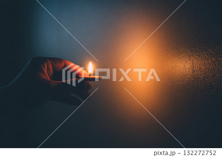 Single hand holding lit candle in quiet, dimly lit room creates warm, peaceful atmosphere with soft shadows on smooth wall, evoking calm and solitude Single hand holding lit candle in quiet, dimly lit room creates warm, peaceful atmosphere with soft shadows on smooth wall, evoking calm and solitude 132272752