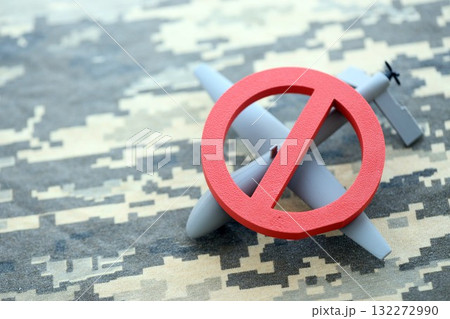 Unnamed grey toy drone model and red prohibition sign on camouflage fabric close up. Anti-aircraft warfare concept 132272990