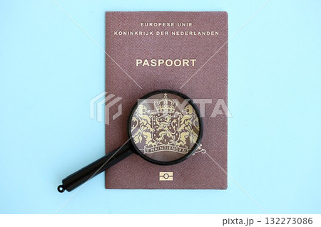 Netherlands passport and magnifying glass on light blue paper background close up. Citizenship details and information concept Netherlands passport and magnifying glass on light blue paper background close up. Citizenship details and information concept 132273086