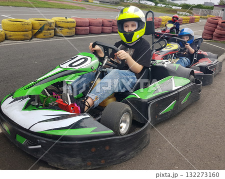 A cute child wearing a yellow helmet enjoying a thrilling ride on a karting track  132273160