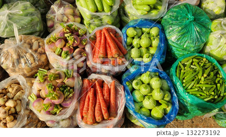 A vibrant assortment of fresh vegetables displayed in plastic bags at a market including carrots okra shallots and other greens showcasing variety and freshness 132273192
