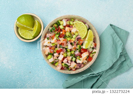 Peruvian seafood ceviche with shrimps, octopus, tomatoes, cucumber, and parsley in a bowl served with lime top view Peruvian seafood ceviche with shrimps, octopus, tomatoes, cucumber, and parsley in a bowl served with lime top view 132273224