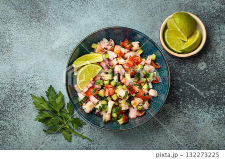 Peruvian seafood ceviche with shrimps, octopus, tomatoes, cucumber, and parsley in a bowl served with lime top view Peruvian seafood ceviche with shrimps, octopus, tomatoes, cucumber, and parsley in a bowl served with lime top view 132273225