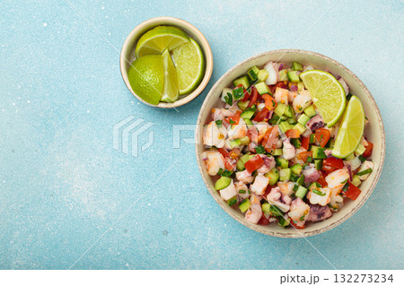 Peruvian seafood ceviche with shrimps, octopus, tomatoes, cucumber, and parsley in a bowl served with lime top view, space for text Peruvian seafood ceviche with shrimps, octopus, tomatoes, cucumber, and parsley in a bowl served with lime top view, space for text 132273234