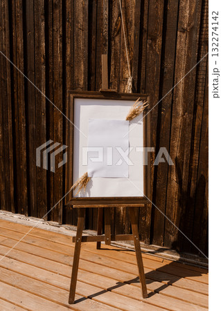 Rustic Wedding Easel with Blank Paper, Pampas Grass, and Wooden Barn Backdrop Warm Tones, Natural Decor, Ceremony Signage, Outdoor Event. Rustic Wedding Easel with Blank Paper, Pampas Grass, and Wooden Barn Backdrop Warm Tones, Natural Decor, Ceremony Signage, Outdoor Event. 132274142
