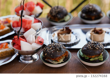 Gourmet Black Burger Bites with Watermelon Skewers on Silver Platters, Outdoor Catering, Rustic Style Food Photography, Vibrant Colors. Gourmet Black Burger Bites with Watermelon Skewers on Silver Platters, Outdoor Catering, Rustic Style Food Photography, Vibrant Colors. 132274168