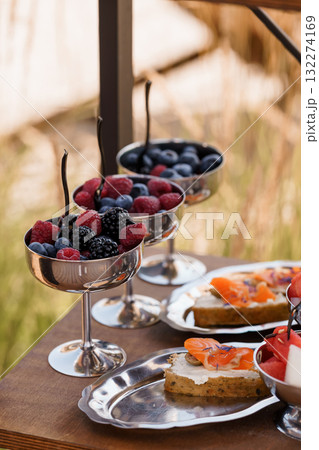 Elegant Outdoor Brunch Setup with Silverware, Berries, and Salmon Tartlets, Rustic Table, Warm Light, and Natural Background Elegant Outdoor Brunch Setup with Silverware, Berries, and Salmon Tartlets, Rustic Table, Warm Light, and Natural Background 132274169