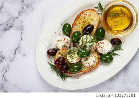 a plate with a snack, ciabatta bread with cheese and olives, olive oil, spices and herbs, top view, no people, a plate with a snack, ciabatta bread with cheese and olives, olive oil, spices and herbs, top view, no people, 132275201