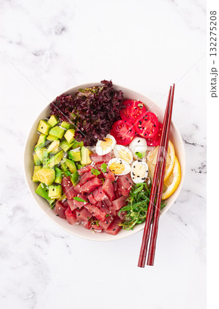 Fresh poke bowl, with tuna, avocado, and vegetables, served on a white plate Fresh poke bowl, with tuna, avocado, and vegetables, served on a white plate 132275208