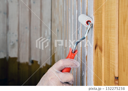 Applying white paint to vertical wooden wall slats with roller. Applying white paint to vertical wooden wall slats with roller. 132275238