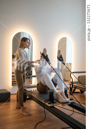 Woman Pilates Instructor Gives Guidance to a men Student While They Utilize the Reformers Equipment Woman Pilates Instructor Gives Guidance to a men Student While They Utilize the Reformers Equipment 132275671