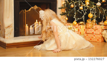 Happy little girl child with festive gift box sitting near Christmas tree and fireplace at home Happy little girl child with festive gift box sitting near Christmas tree and fireplace at home 132276027