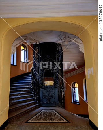 An old circular elevator cage stands beside a curved marble staircase in a classic St. Petersburg entrance hall. 132276047
