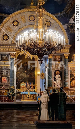 A wedding ceremony taking place beneath a huge golden chandelier inside the richly decorated St. Petersburg cathedral. A wedding ceremony taking place beneath a huge golden chandelier inside the richly decorated St. Petersburg cathedral. 132276156
