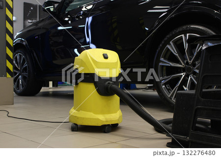 A yellow vacuum cleaner near a car on the garage floor before cleaning A yellow vacuum cleaner near a car on the garage floor before cleaning 132276480