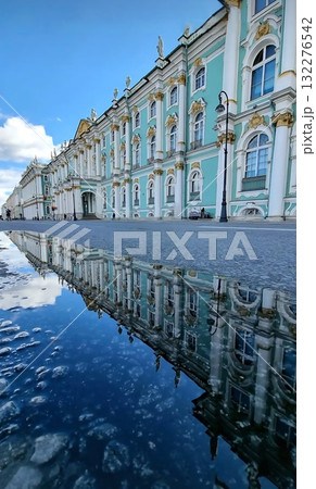 The focus is on the reflection of the Winter Palace, which is seen in a deep puddle on the wet pavement. The majestic baroque building with its columns and white trim is perfectly mirrored under a blu The focus is on the reflection of the Winter Palace, which is seen in a deep puddle on the wet pavement. The majestic baroque building with its columns and white trim is perfectly mirrored under a blu 132276542