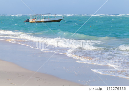 A small motor boat floats off a white sandy beach as turquoise waves A small motor boat floats off a white sandy beach as turquoise waves 132276586