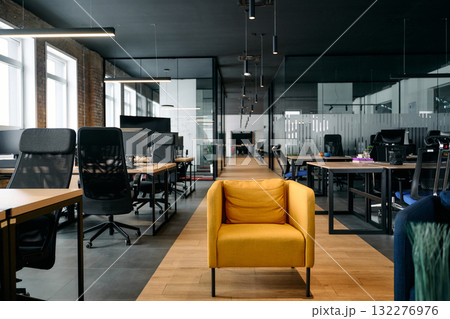 Contemporary open space office interior with minimalist design, black chairs, wooden desks, and glass partitions, representing a professional corporate workspace environment. 132276976