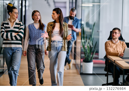 Group of coworkers walking and discussing ideas in a modern office corridor while a male colleague works at a laptop nearby, symbolizing teamwork, productivity, and creative collaboration in a Group of coworkers walking and discussing ideas in a modern office corridor while a male colleague works at a laptop nearby, symbolizing teamwork, productivity, and creative collaboration in a 132276984