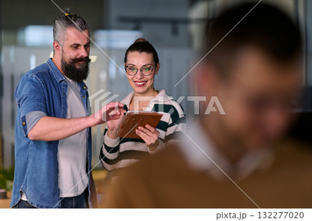 Two cheerful coworkers collaborating and sharing ideas using a digital tablet in a modern office, symbolizing teamwork, creativity, and communication in a professional business environment. 132277020