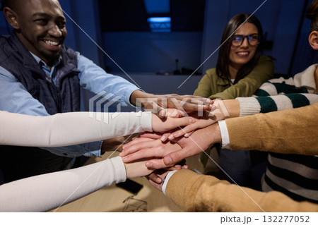 Top view of diverse coworkers business people joining hands together over a wooden office desk, symbolizing teamwork, unity, collaboration, and support in a modern workplace. 132277052