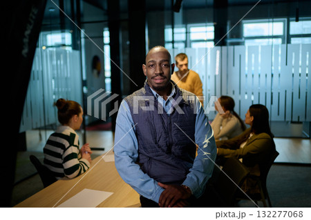 Portrait of a confident african american businessman in a modern office with colleagues discussing in the background, symbolizing leadership, teamwork, success, and collaboration in a corporate Portrait of a confident african american businessman in a modern office with colleagues discussing in the background, symbolizing leadership, teamwork, success, and collaboration in a corporate 132277068