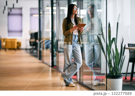 Professional business woman standing in modern office corridor, holding digital tablet and smiling confidently, representing leadership, technology, and success in a creative business environment. Professional business woman standing in modern office corridor, holding digital tablet and smiling confidently, representing leadership, technology, and success in a creative business environment. 132277089