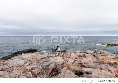 Couple in love, a man and a woman are sitting on a rocky seashore Couple in love, a man and a woman are sitting on a rocky seashore 132277673