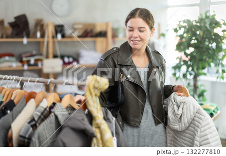 Stylish young girl standing in clothing shop and looking new down jacket made of high-quality material. Shopping and seasonal sales concept, winter season 132277810