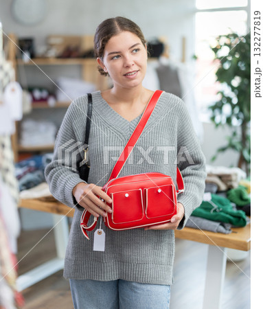 Positive young girl choosing handbag in clothing store 132277819