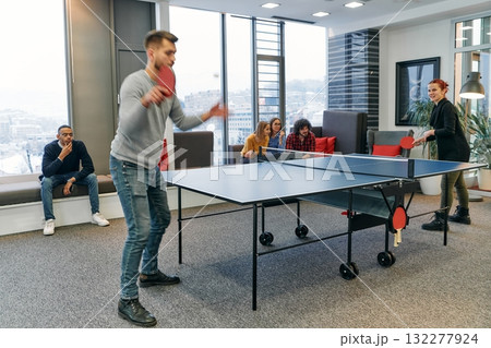 Business colleagues take a break from work to enjoy a game of table tennis, fostering teamwork and camaraderie in the workplace 132277924