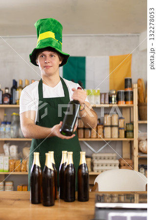 Positive male store clerk in green hat is preparing to meet customers on eve of St. Patricks Day. 132278053