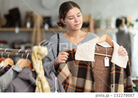 Young woman chooses plaid jacket in clothing store Young woman chooses plaid jacket in clothing store 132278087