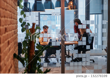 In a sleek glass office space, a team of business professionals engage in lively discussions and exchange strategic ideas, showcasing collaboration and innovation at the heart of modern corporate 132278109