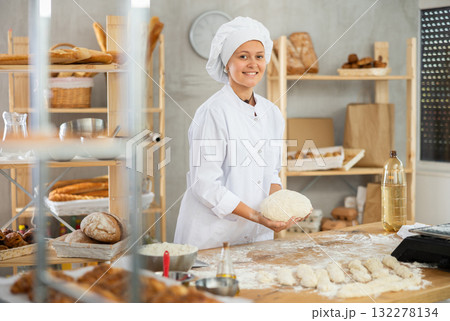 Working in bakery - girl kneads raw dough to make baguettes or croissants Working in bakery - girl kneads raw dough to make baguettes or croissants 132278134