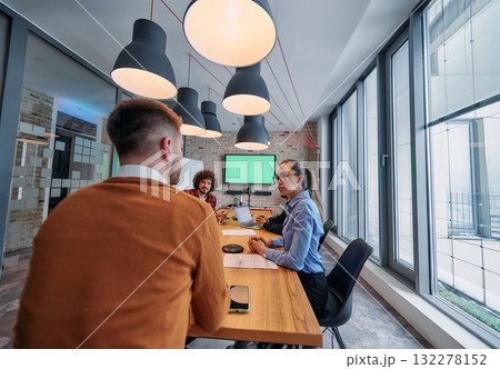 In the vibrant ambiance of a modern startup office, a diverse team of business professionals engage in discussions on various projects and develop new business strategies, epitomizing creativity and 132278152