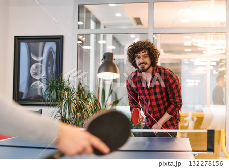 Business colleagues take a break from work to enjoy a game of table tennis, fostering teamwork and camaraderie in the workplace 132278156