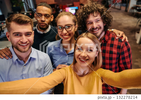A diverse group of business professionals take a break from their tasks in a modern startup office to capture a creative selfie, showcasing teamwork and a vibrant workplace culture 132278214