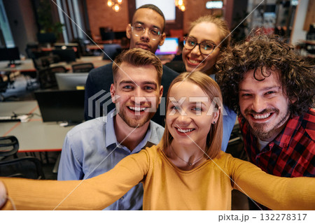 A diverse group of business professionals take a break from their tasks in a modern startup office to capture a creative selfie, showcasing teamwork and a vibrant workplace culture 132278317