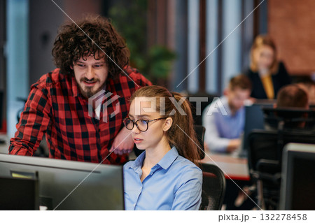 Business colleagues, a man and a woman, engage in discussing business strategies while attentively gazing at a computer monitor, epitomizing collaboration and innovation 132278458