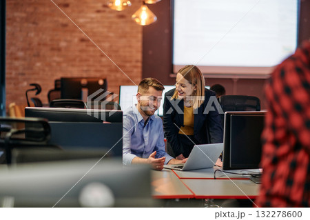Business colleagues, a man and a woman, engage in discussing business strategies while attentively gazing at a computer monitor, epitomizing collaboration and innovation 132278600